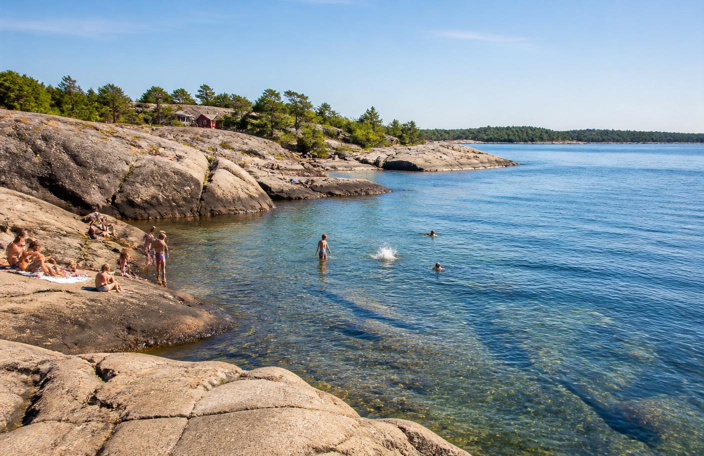 Badande på släta granithällar vid Grisslehamn med turkosblått hav