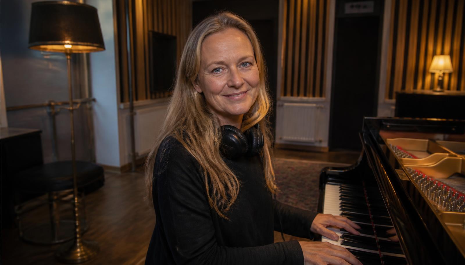 Jennie Löfgren sitter vid flygeln i en studio och ler mot kameran