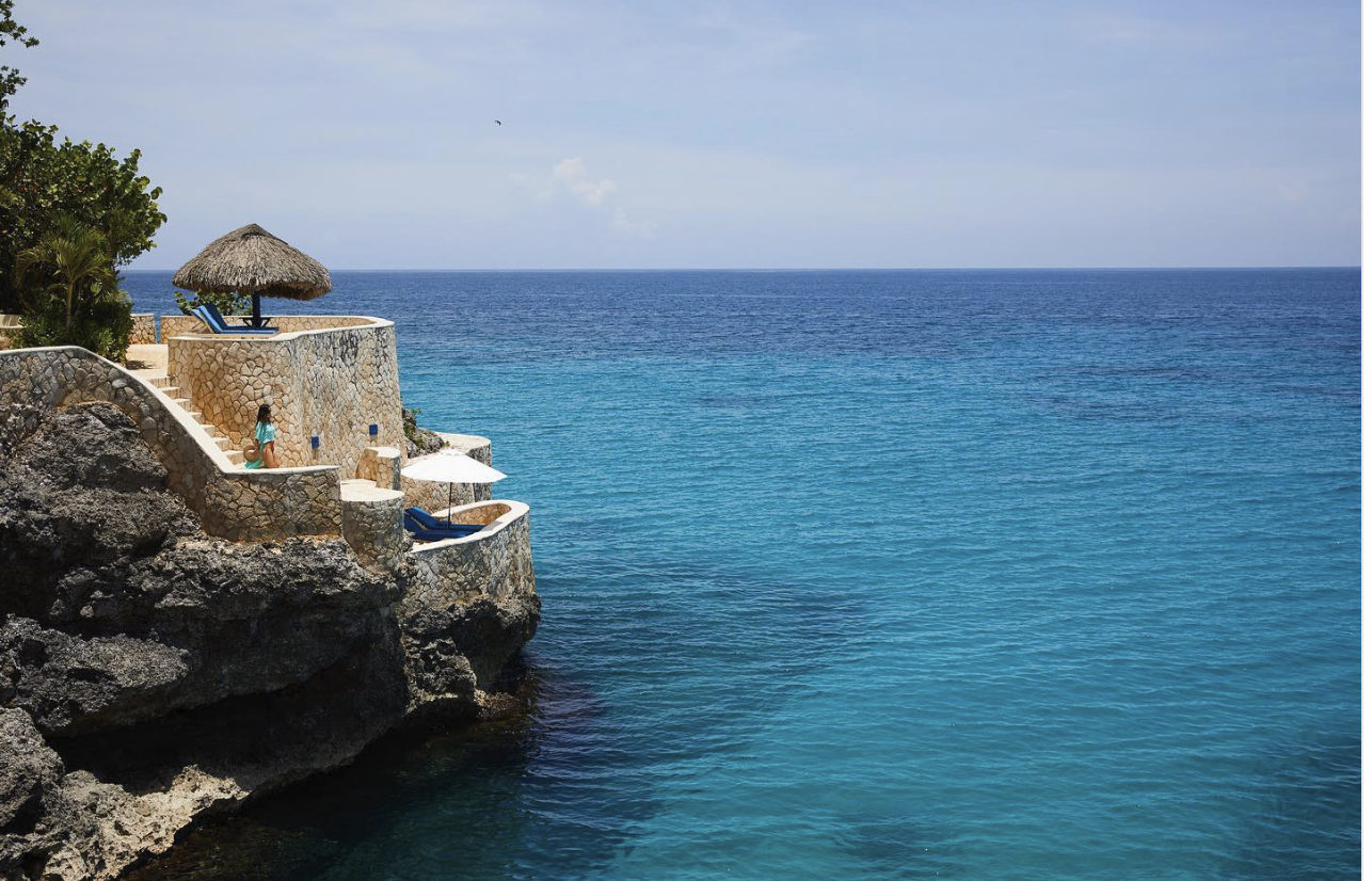 Stentrappor och solstolar på klipporna vid The Caves i Negril mot ett turkost hav