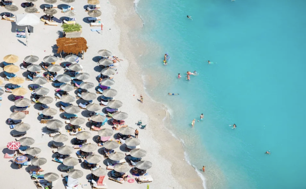 Flygbild över strand i Albanien med rader av parasoller och turkost vatten