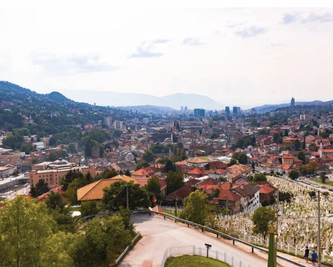 Vy över Sarajevo från en höjd med röda tak, minareter och berg i bakgrunden