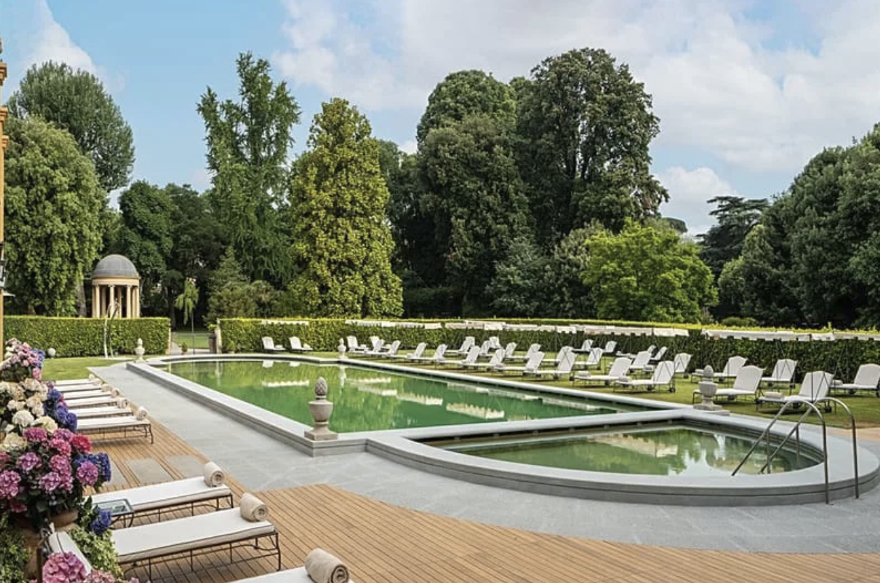 Elegant hotellpool omgiven av solstolar, häckar och träd
