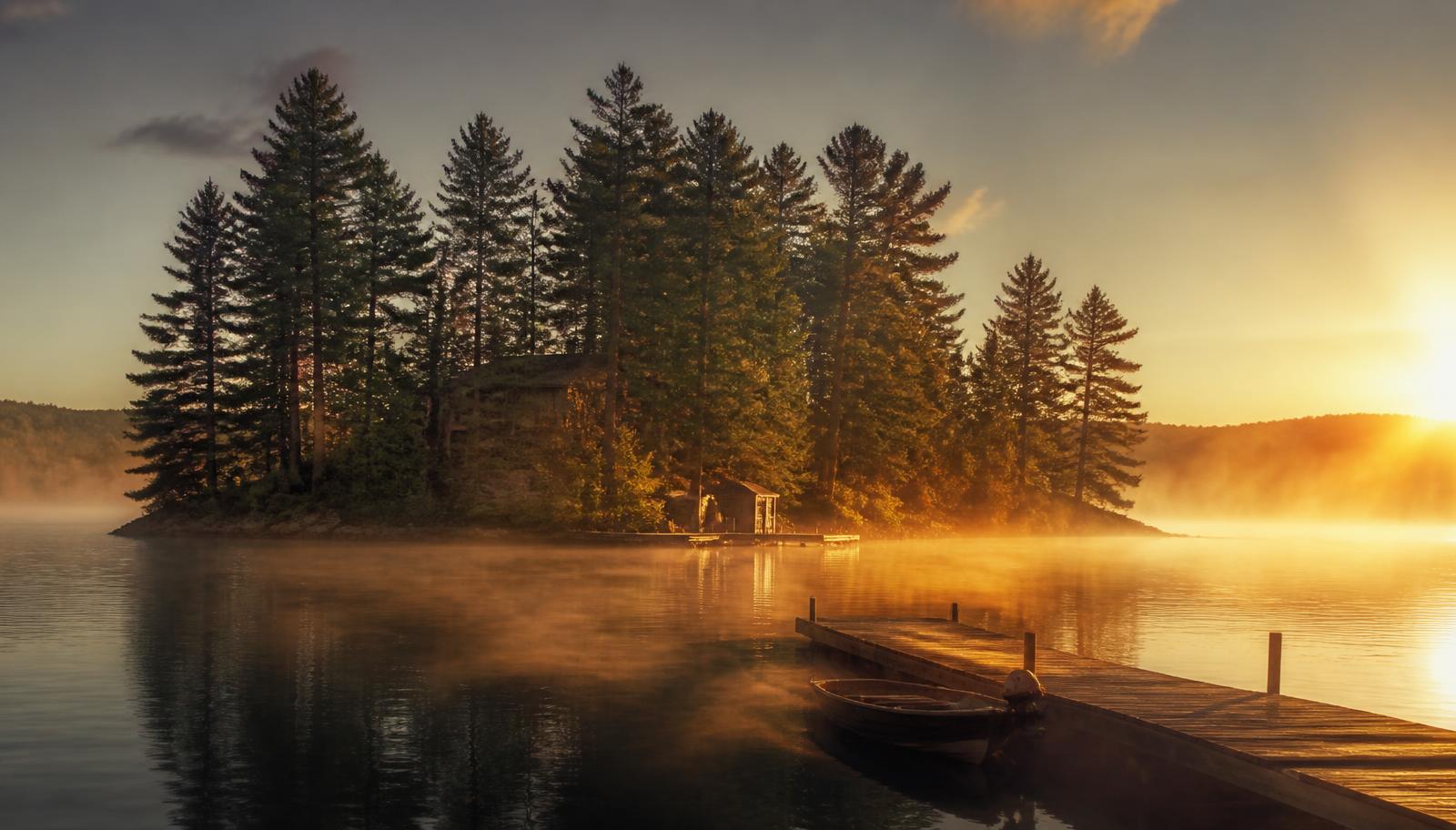 Dimmig skogsö i en kanadensisk sjö i gyllene morgonljus med brygga och eka